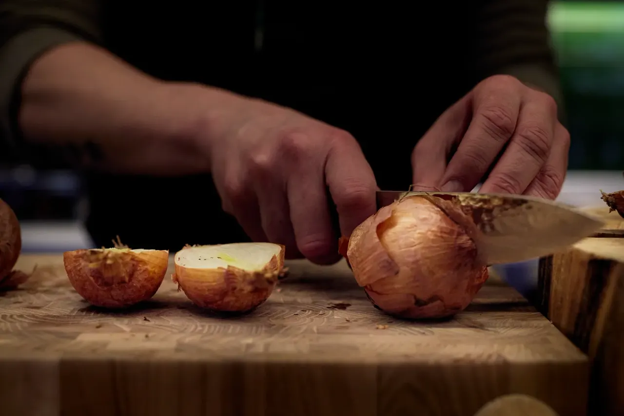 Manos del equipo cortando cebolla asada sobre la tabla de trabajo de la cocina de El Invernadero