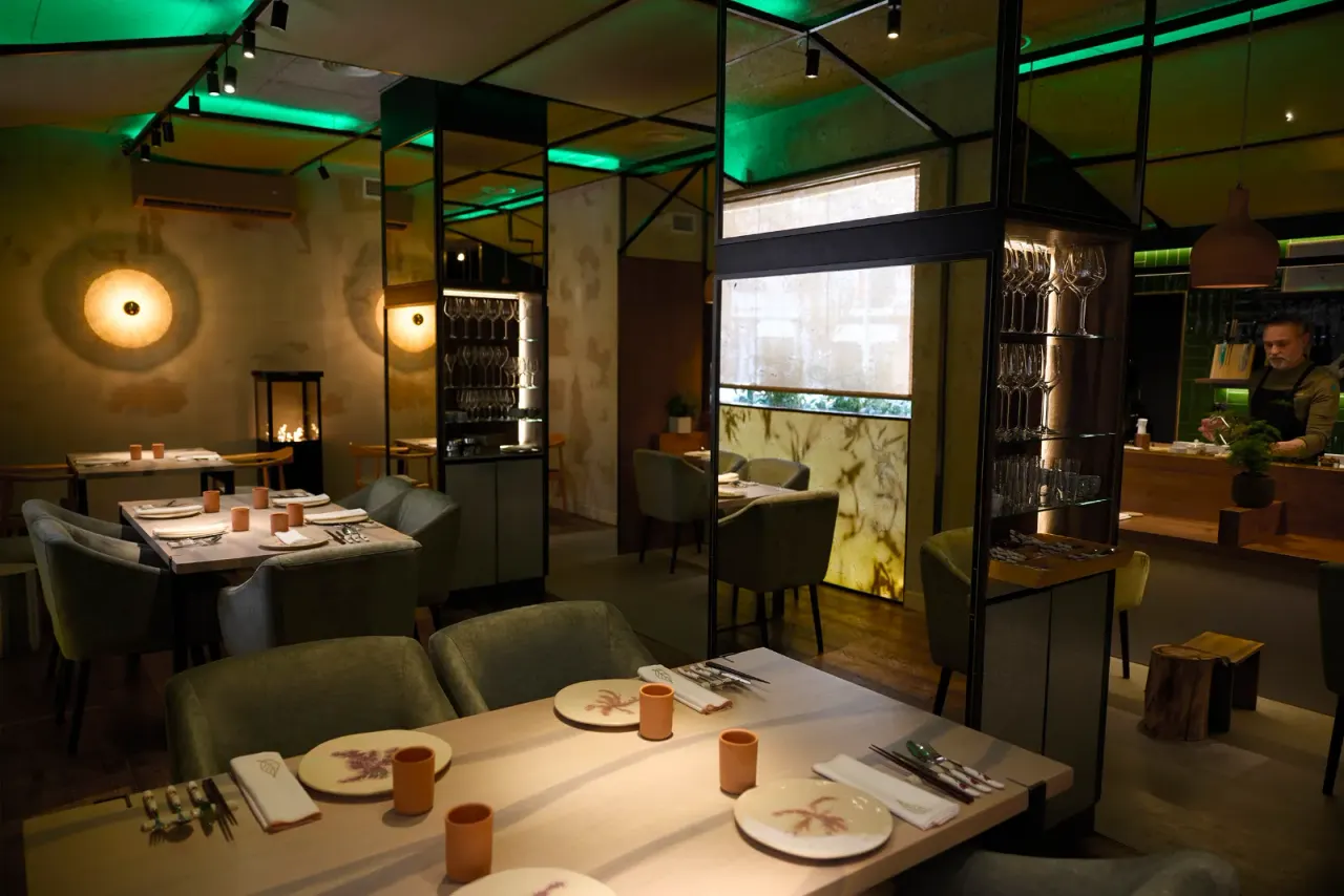 Comedor de El Invernadero con las mesas vestidas y la ventana con vegetación al fondo
