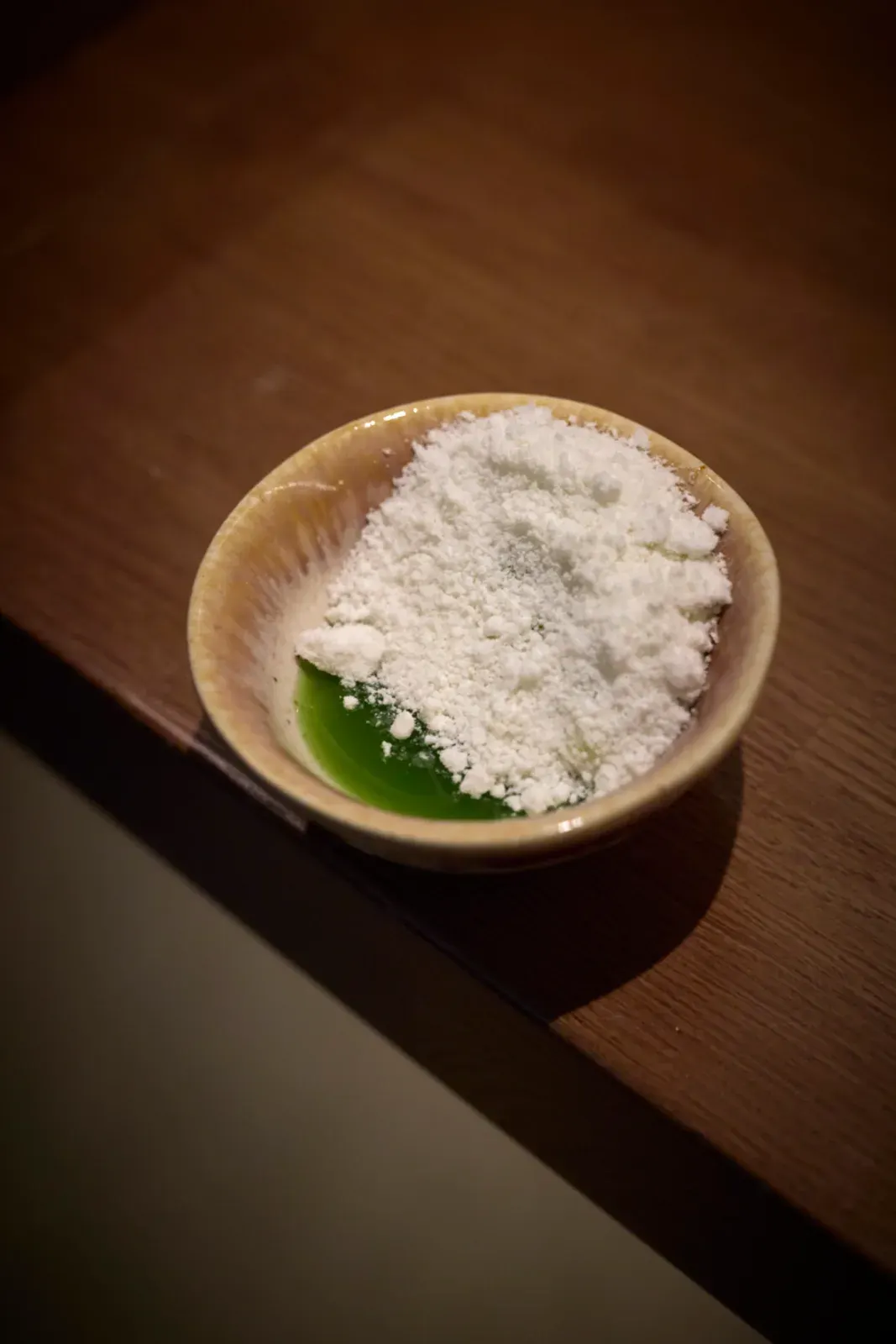 Cuenco con un polvo blanco y una hoja verde fresca, preparado en el pase