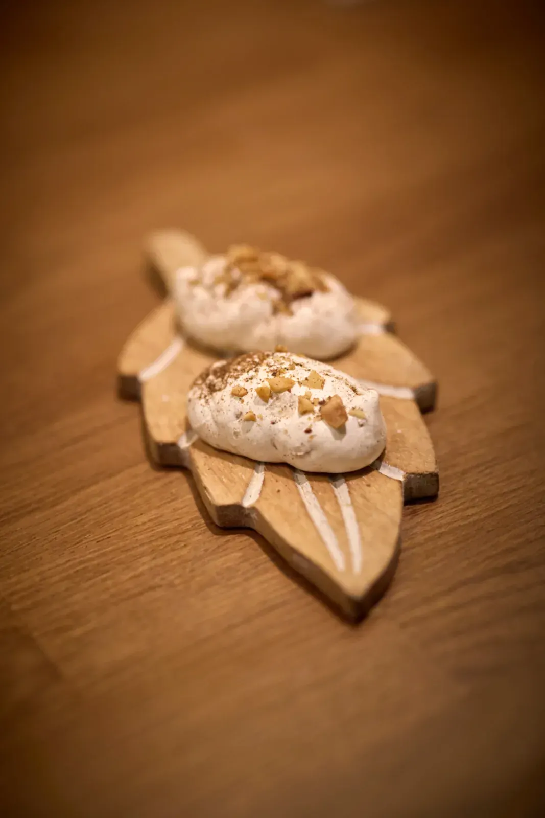 Dos bocados blancos con trocitos dorados por encima, sobre una tabla de madera con forma de hoja
