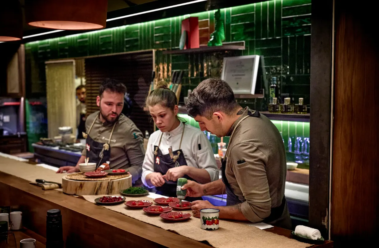 Tres cocineros emplatando a la vez en fila, en la cocina vista de El Invernadero