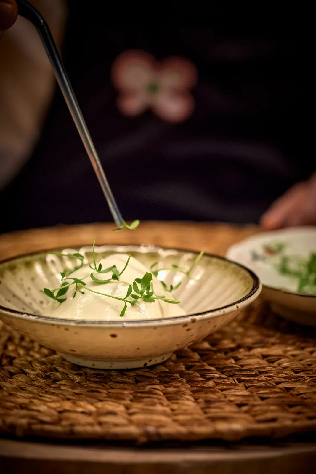 Unas pinzas rematan con brotes verdes una crema clara servida en cuenco de cerámica
