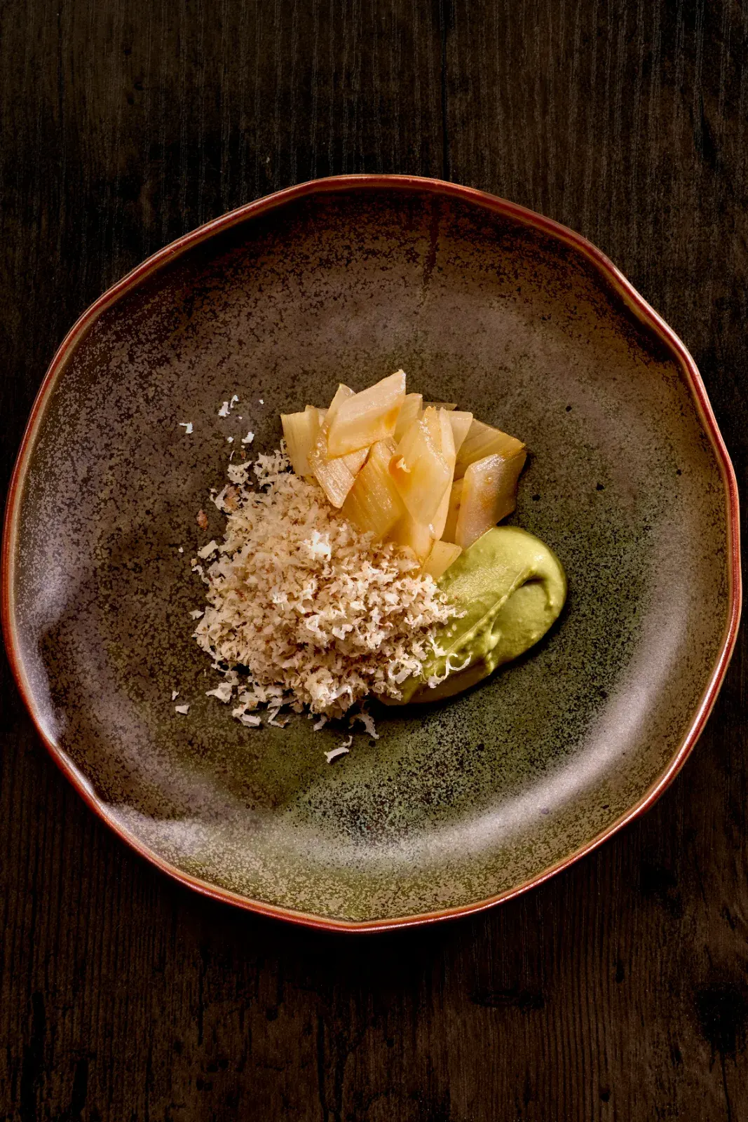 Apio con té y nuez: crema verde, láminas y crumble en plato de cerámica