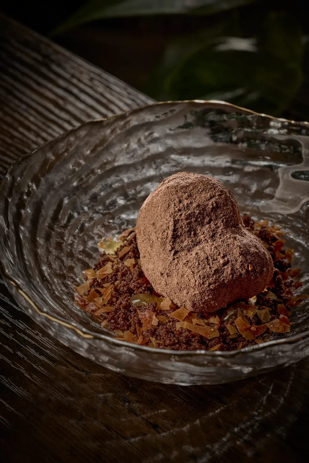 Bocado espolvoreado de cacao sobre su crumble y unas láminas ámbar, en cuenco de cristal de borde dorado