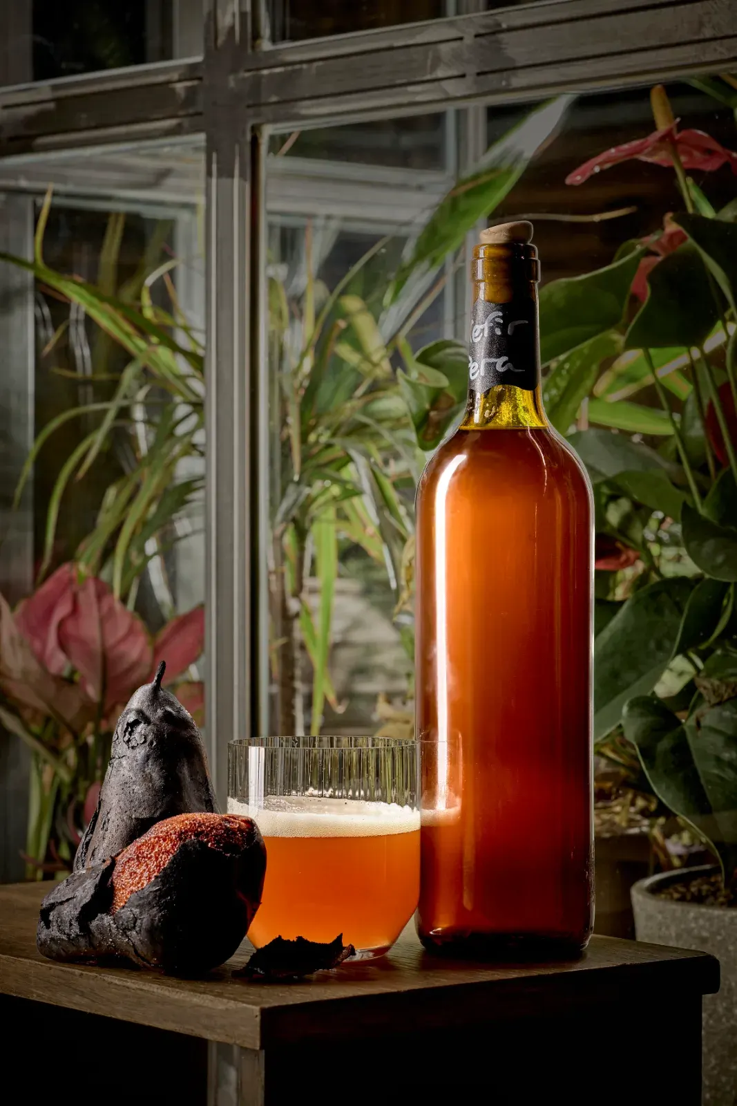 Botella y vaso de kéfir de pera embotellado en la casa, entre las plantas del comedor