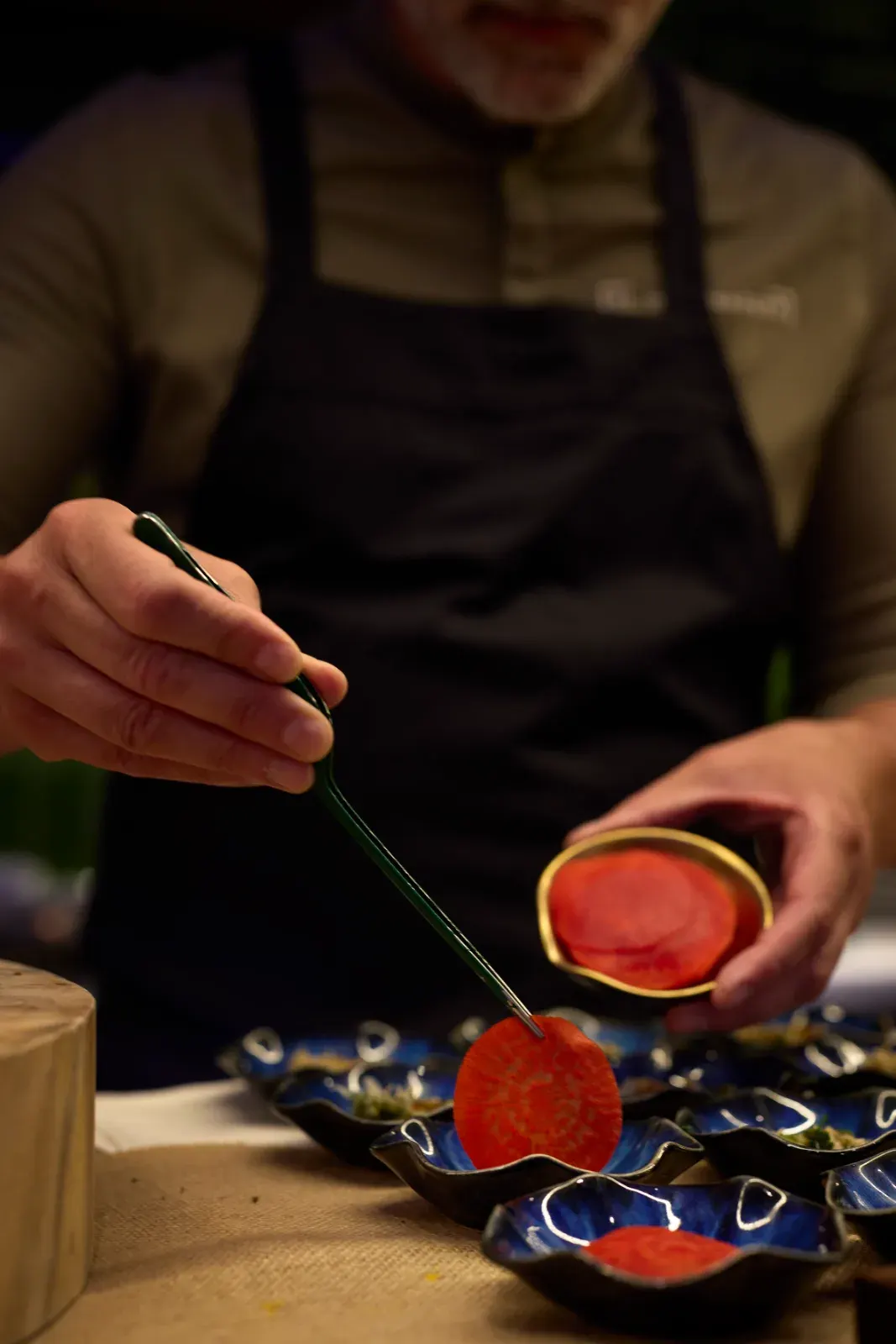Un cocinero coloca con pinzas láminas rojas sobre una fila de platos azules, durante el emplatado